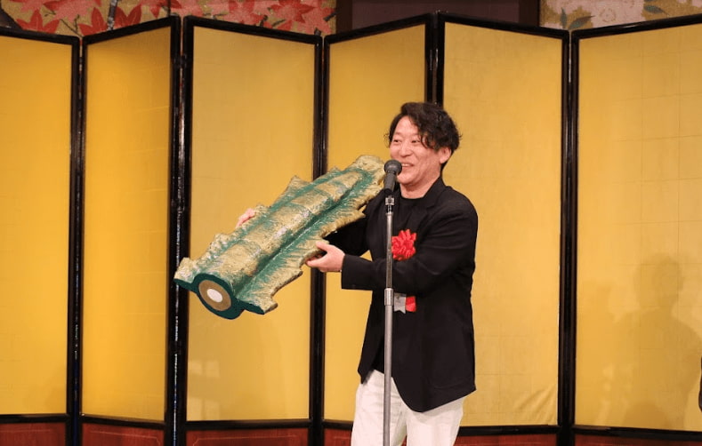 写真 人物 金龍ラーメンの尻尾を持って挨拶する宮原広志氏