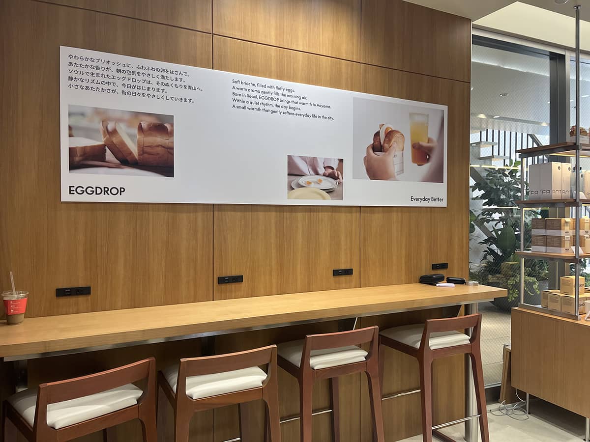 店舗デザインは、ソウル本店の意匠を踏襲しつつ、日本の生活者が好む落ち着いた雰囲気に合わせた。「静けさと温かさ」をテーマに、自然光が入り込む曲面ガラスや木の質感を活かした内装を採用。カウンター席やボックス席など、さまざまな利用シーンに対応する設計となっている。朝の一人利用から週末のブランチまで、幅広い客層を想定した空間だ。